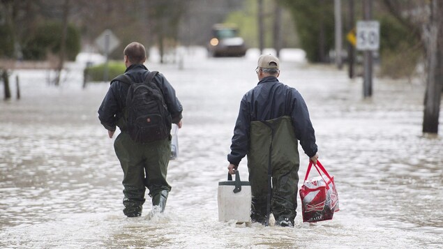 Deux hommes transportent certaines de leurs possessions dans une rue inondée de Rigaud.