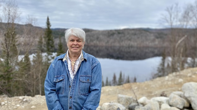 Une femme sourit devant un lac au printemps.