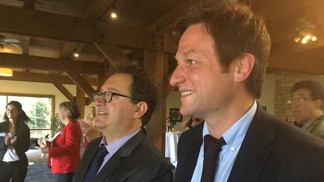 Deux hommes souriants, en costume-cravate, sont photographiés de profil.