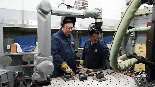 Deux soudeurs devant un bras robotisé.