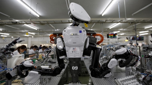 Un robot doté de deux bras et de ce qui ressemble à une tête, dans une manufacture. Un robot doté de deux bras et de ce qui ressemble à une tête, dans une manufacture.