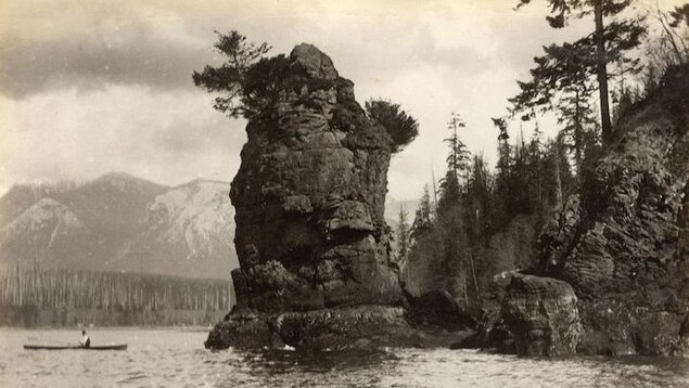 Une personne dans un canot se promène sur l'eau près d'un grand rocher avec montagnes en toile de fond Une personne dans un canot se promène sur l'eau près d'un grand rocher avec montagnes en toile de fond