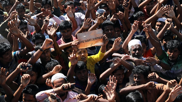Une foule d'hommes dont la plupart ont les bras levés. Un de ceux-ci portent une pancarte portant l'inscription « We want justice» (Nous voulons que justice soit faite».