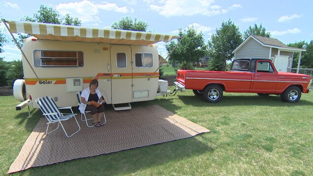 Une dame lit un magasine sur une chaise de camping installée devant sa caravane Boler, cette dernière étant attachée à son pick-up. Une dame lit un magasine sur une chaise de camping installée devant sa caravane Boler, cette dernière étant attachée à son pick-up.