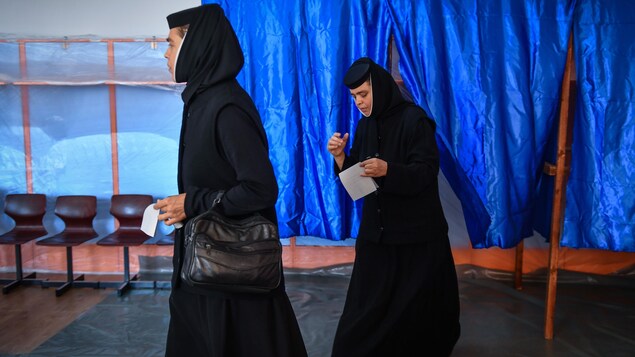 Deux religieuses vêtus d'habits religieux sortent de l'isoloir avec leur papier de vote en main