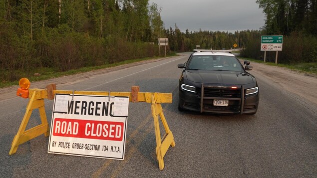 Une autopatrouille et ue barrière sur laquelle on peut lire « Fermeture d'urgence » avec la forêt en arrière-plan.