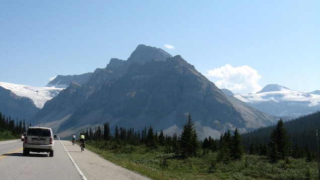 Des voitures et des cyclistes sur une route au milieu des montagnes Des voitures et des cyclistes sur une route au milieu des montagnes