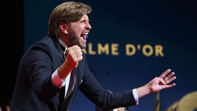 Le réalisateur célèbre sa victoire au micro du Festival de Cannes. Les mots « Palme d'or » apparaissent sur un écran derrière lui.