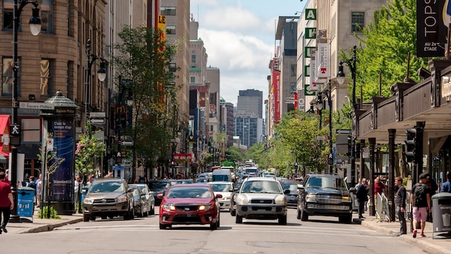 Des voitures et des piétons circulent sur une rue commerciale au centre-ville de Montréal.