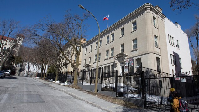 Deux piétons longent la grille devant le consulat de Russie à Montréal.