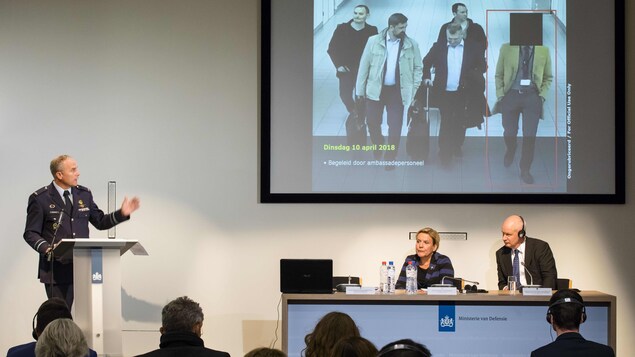 Ank Bijleveld, Onno Eichelsheim et Peter Wilson participent à une conférence de presse. Sur un écran derrière eux est projetée la photo de passeport d'un suspect russe.