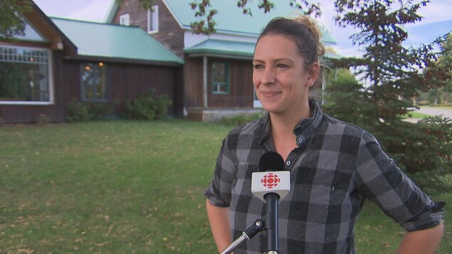 Ruth Ellen Brosseau, les mains sur les hanches, en chemise à carreaux, devant un micro de Radio-Canada.