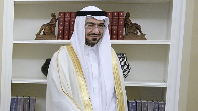 Un homme portant l'habit traditionnel saoudien et des lunettes en face d'une bibliothèque.