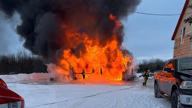 Des flammes couvrent un garage dans sa totalité. Un pompier se déplace vers l'incendie.