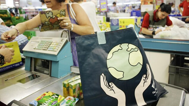 Une dame utilise un sac en plastique réutilisable sur lequel on peut voir la Terre tenue par deux mains. Une dame utilise un sac en plastique réutilisable sur lequel on peut voir la Terre tenue par deux mains.