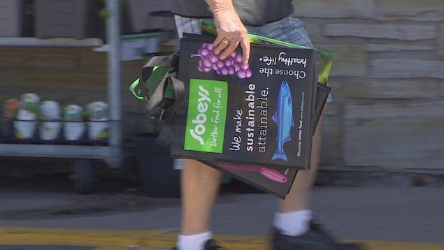 Une personne transporte des sacs réutilisables de marque Sobeys.
