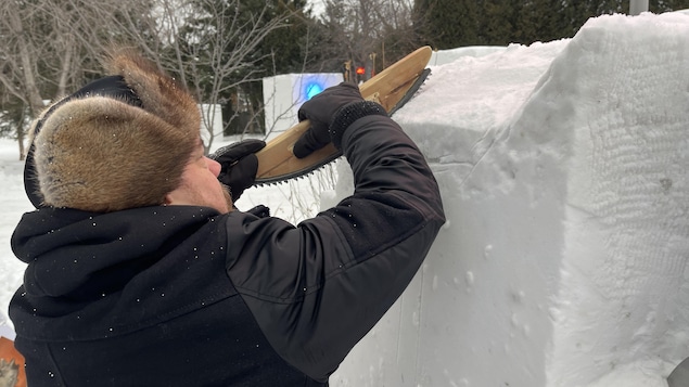 Un sculpteur taille un bloc de neige.