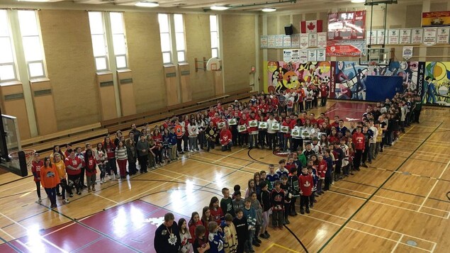 Des centaines de jeunes debout dans un gymnase en formation de H. Des centaines de jeunes debout dans un gymnase en formation de H.