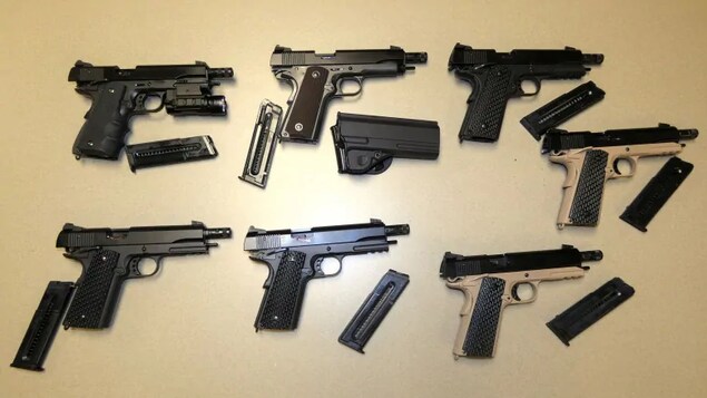 Six armes à feu illégales sont étendues sur une table.