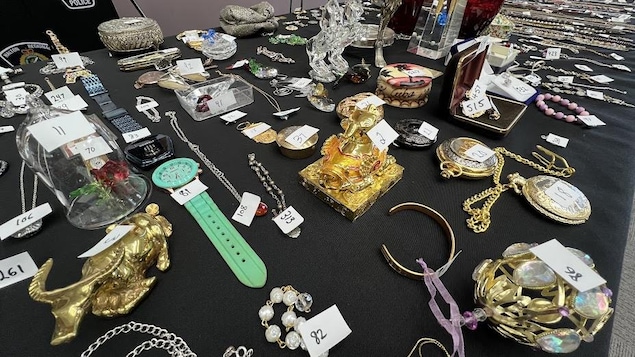 Une table avec une nappe noire où des bijoux, des bibelots, des urnes et divers objets de valeurs sont disposés et numérotés.