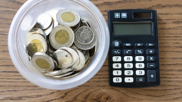Des pièces de 2 dollars canadiens et d'autres pièces de monnaie dans un contenant de plastique posé à côté d'une calculatrice.