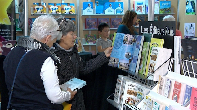 Deux femmes feuillètent des romans à un kiosque dans un salon du livre. 