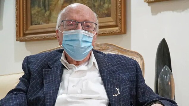 Un homme âgé assis sur une chaise et portant un masque.