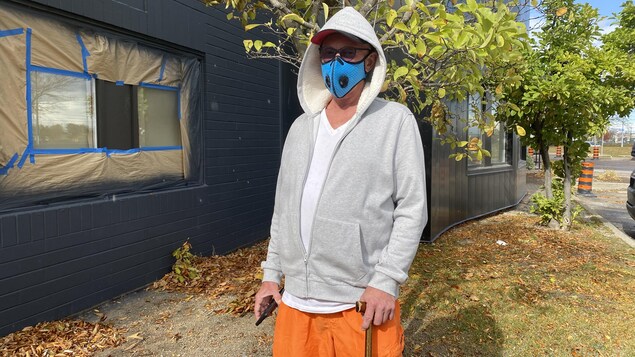 Un homme avec une canne et des shorts orange. Il porte également un couvre-visage bleu.