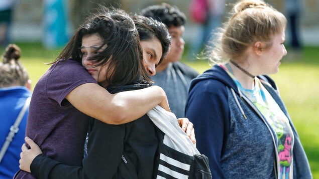 Une fille et un garçon se serrent dans leur bras à l'extérieur. D'autres personnes se trouvent autour d'eux et regardent au loin. Une fille et un garçon se serrent dans leur bras à l'extérieur. D'autres personnes se trouvent autour d'eux et regardent au loin.