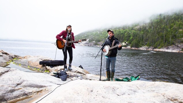 Deux musiciens sur des roches près de l'eau. 