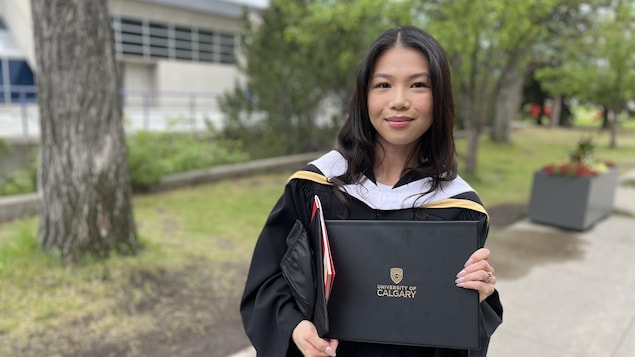 Sarah Chung en toge universitaire tient son diplôme.