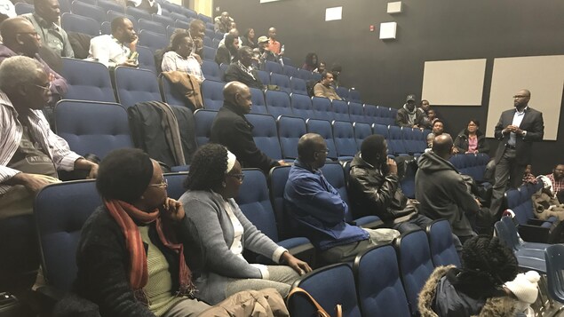 Une cinquantaine de personnes sont assises dans un amphithéâtre et écoutent un homme qui est debout.