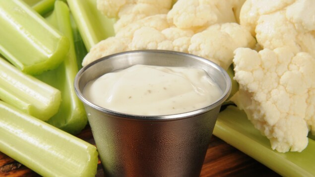 Un petit récipient contenant de la sauce ranch, entouré de légumes crus.