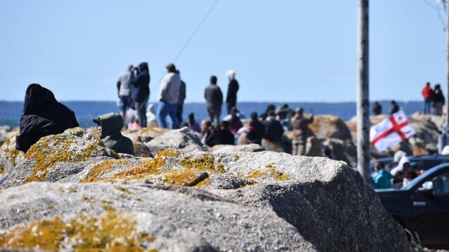 Des gens près des rochers. Un drapeau mi'kmaq flotte.