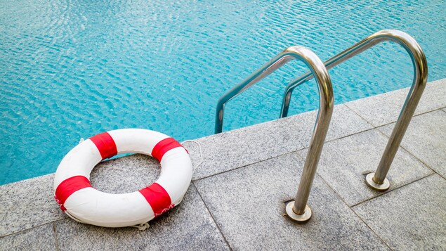 Une bouée est déposée sur le béton entourant une piscine, à gauche de l'échelle.
