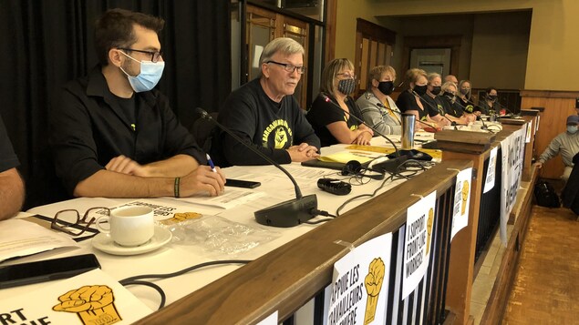 Une table de conférence de presse avec une dizaines d'individus du Syndicat canadien de la fonction publique pour le Nouveau-Brunswick.