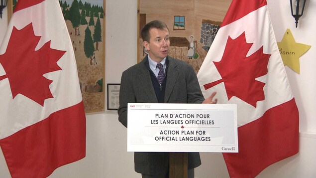 Scott Brison devant une affiche qui indique « Plan d'action pour les langues officielles ». Scott Brison devant une affiche qui indique « Plan d'action pour les langues officielles ».