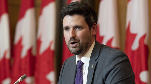 Sean Fraser nagsasalita habang may mga watawat ng Canada sa kanyang likuran.