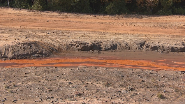 Un ruisseau à la couleur orange au milieu d'un terrain vague.