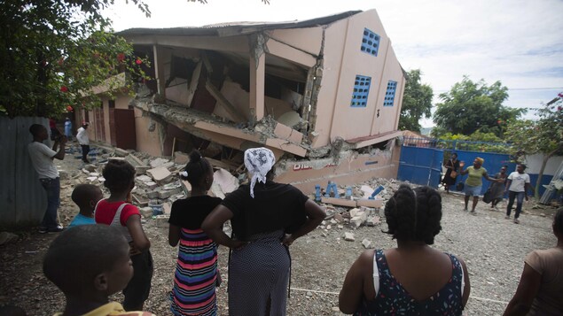 Plusieurs passants regardent une école effondrée