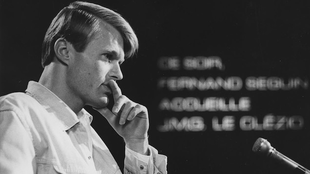 Dans un studio de télévision, l'écrivain Jean-Marie Gustave Le Clézio, lors d'une entrevue. Un micro de table est posé devant lui.