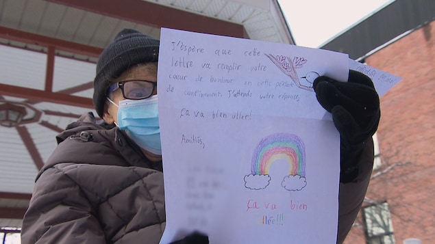 Une dame âgée qui lit une lettre d'un enfant sur laquelle on voit un arc-en-ciel dessiné.