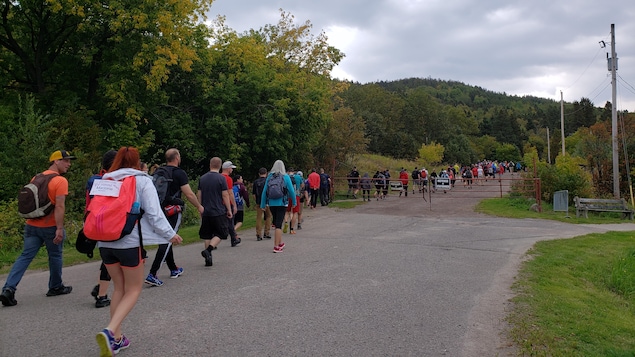 Cent personnes marchent l'une derrière l'autre dans un sentier dans le bois.