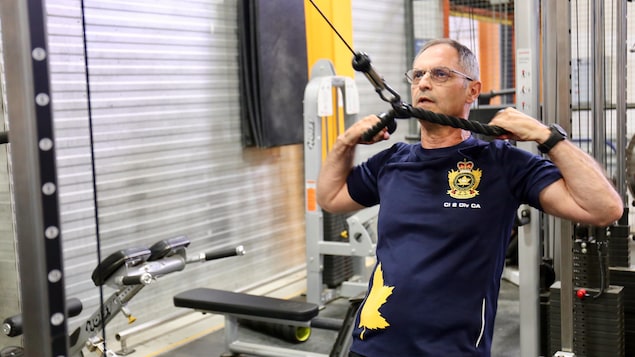Un homme dans la cinquantaine s'entraîne dans un gym. Il tire sur une corde tendue pour soulever des poids et muscler ses bras et ses épaules. Un homme dans la cinquantaine s'entraîne dans un gym. Il tire sur une corde tendue pour soulever des poids et muscler ses bras et ses épaules.