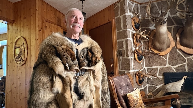 Serge Guitard vêtu d'un manteau en peaux de coyote pose pour la photo dans son salon.