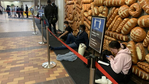 Des gens en file d'attente, certains sont assis. 