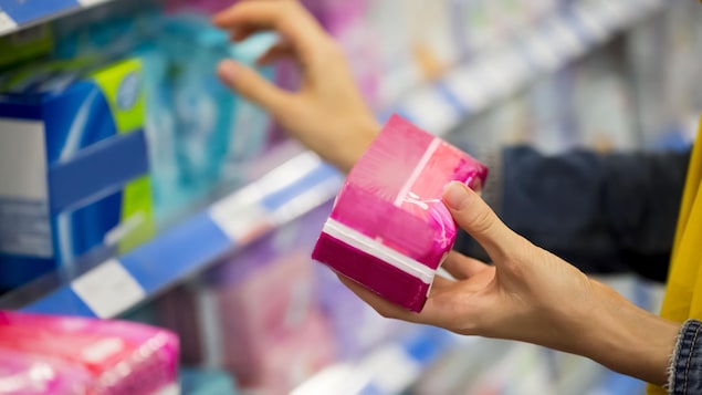Une femme tient un paquet de serviettes hygiéniques dans un supermarché.