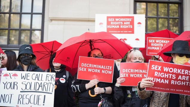 Sex workers and their supporters gather outside the Ontario Superior Court, holding signs and umbrellas.