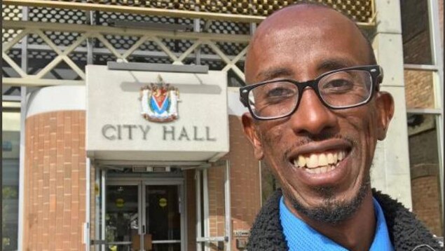 Gros plan sur le visage de Sharmarke Dubow qui sourit devant l'hôtel de ville de Victoria.