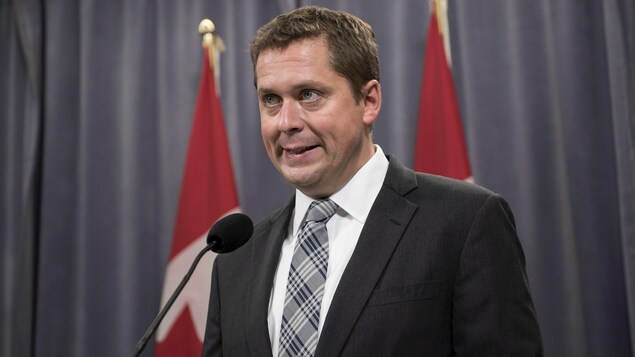 Le chef conservateur Andrew Scheer lors du congrès national de son parti à Halifax. Il parle dans un micro. Derrière lui deux drapeaux canadiens. Le chef conservateur Andrew Scheer lors du congrès national de son parti à Halifax. Il parle dans un micro. Derrière lui deux drapeaux canadiens.